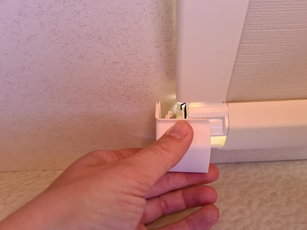 Hand h&auml;lt wei&szlig;en Kunststoffhalter an der Endkappe einer Faltstore-Schiene unter der Decke