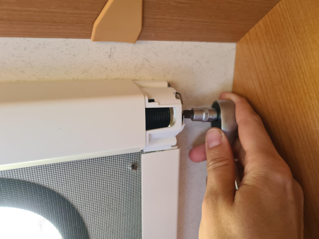 Hand h&auml;lt einen runden Metallaufsatz an der Seite eines wei&szlig;en Metallgeh&auml;uses mit Gitter, unter einem Holzschrank