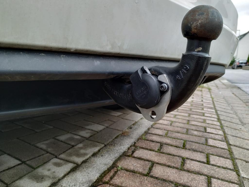 Anh&auml;ngerkupplung mit Kugelkopf und Steckdose unter der Hecksto&szlig;stange eines wei&szlig;en Fahrzeugs, gepflasterter Boden