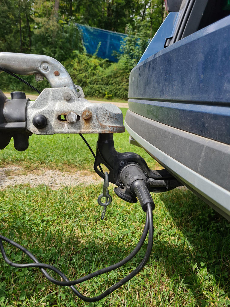 Anh&auml;ngerkupplung eines Fahrzeugs mit elektrischem Stecker und Kabel, blaue Fahrzeugseite und Gras im Hintergrund