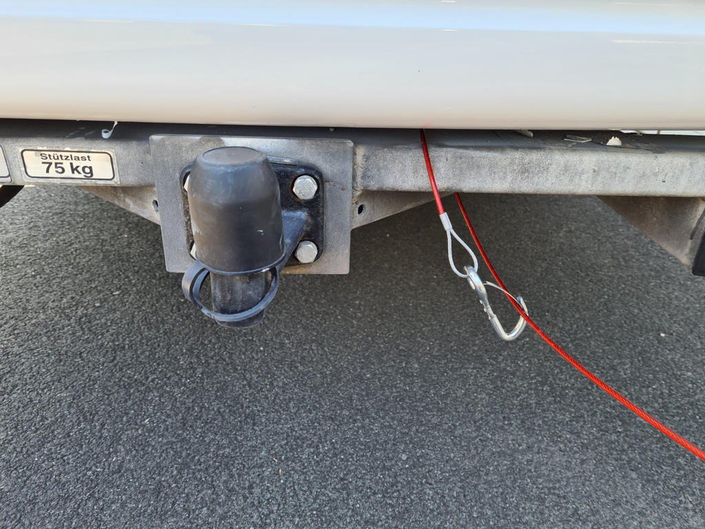 Anh&auml;ngevorrichtung mit schwarzer Kugelabdeckung, Metallrahmen, rotes Sicherungsseil mit Karabiner, Aufkleber '75 kg', Asphalt darunter