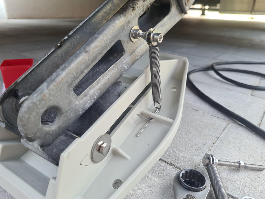 Nahaufnahme eines Metall-Scherenwagenhebers auf einer wei&szlig;en Kunststoffwanne, daneben Stecknuss, Steckschl&uuml;ssel und ein schwarzes Kabel auf Fliesenboden