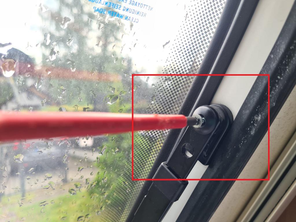 Nahaufnahme eines nassen Fahrzeugfensters mit Regentropfen, ein roter Stab steckt in einer schwarzen Kunststoffbefestigung am Fensterrahmen