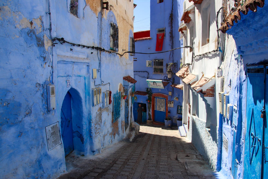 Enge Kopfsteinpflastergasse mit blau und wei&szlig; gestrichenen H&auml;usern, T&uuml;ren, Fenstern, sichtbaren Kabeln und Bereichen mit Licht und Schatten