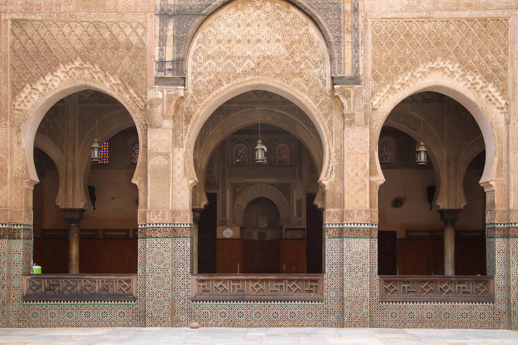 Drei gro&szlig;e geschwungene B&ouml;gen mit verzierten S&auml;ulen, gemusterten Fliesen in der Wandunterseite, h&auml;ngenden Laternen und hellem gepflastertem Boden