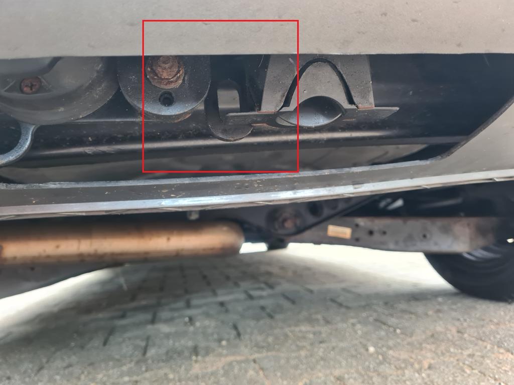 Unterseite eines Fahrzeugs mit Sto&szlig;stangenkante, Auspuffrohr, Metallrahmen und einem roten Rechteck, das einen gebogenen Metallhaken umrahmt