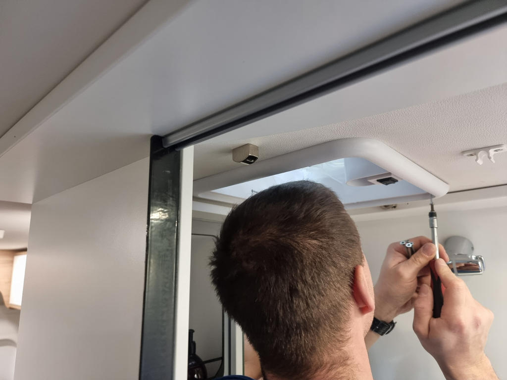 Person von hinten h&auml;lt einen Schraubendreher an eine runde Deckenleuchte in einem Innenraum