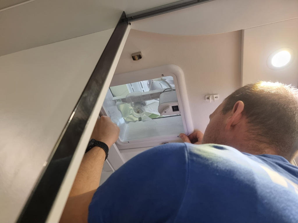 R&uuml;ckenansicht einer Person in blauem T‑Shirt, die eine ge&ouml;ffnete Deckenluke mit sichtbarem Innenraum h&auml;lt; wei&szlig;e Decke mit eingelassenem Licht