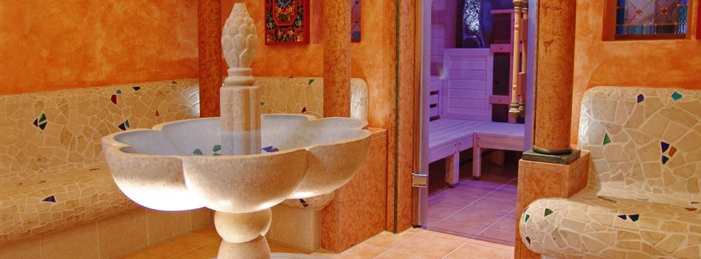 Runde Steinschale auf S&auml;ule mit kleiner Skulptur auf dem Rand, beige-orange geflieste W&auml;nde mit kleinen bunten Mosaikfliesen, geflieste Sitzbank rechts, S&auml;ule neben offenem Durchgang zu einem Raum mit Holzb&auml;nken, gefliester Boden