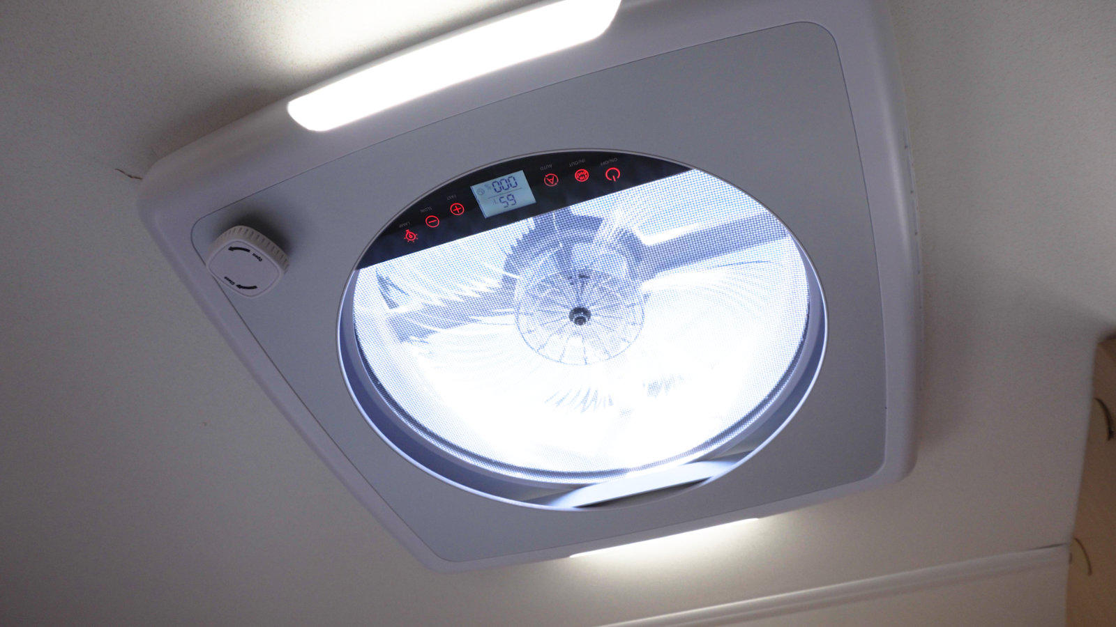 Quadratisches Deckenpaneel mit rundem, durchscheinendem Abdeckfenster; sichtbare L&uuml;fterfl&uuml;gel und Bedienfeld mit roten Leuchtdioden; kleiner runder wei&szlig;er Sensor an der Decke