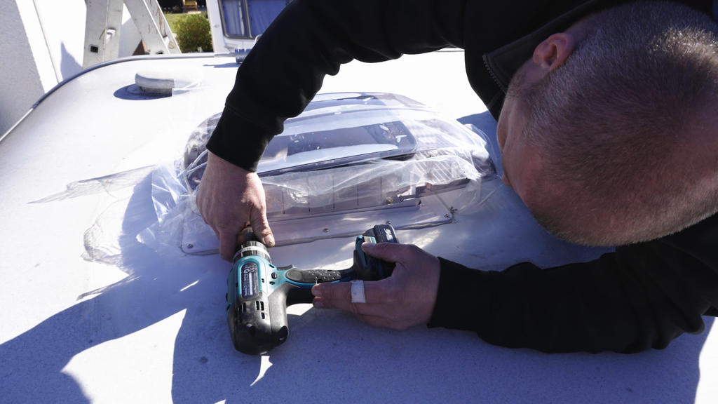 Person beugt sich &uuml;ber eine wei&szlig;e, flache Oberfl&auml;che und h&auml;lt einen Akku-Bohrschrauber neben einer durchsichtigen Plastikfolie