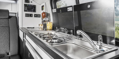 Innenraum mit K&uuml;chenzeile: Edelstahlsp&uuml;le mit Armatur, dreiflammiger Gaskocher, Arbeitsfl&auml;che, Schr&auml;nke, Fenster, Sitzbank und Bedienfeld