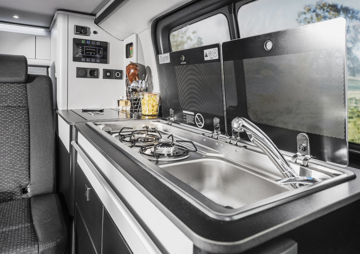 Innenraum mit K&uuml;chenzeile: Edelstahlsp&uuml;le mit Armatur, dreiflammiger Gaskocher, Arbeitsfl&auml;che, Schr&auml;nke, Fenster, Sitzbank und Bedienfeld