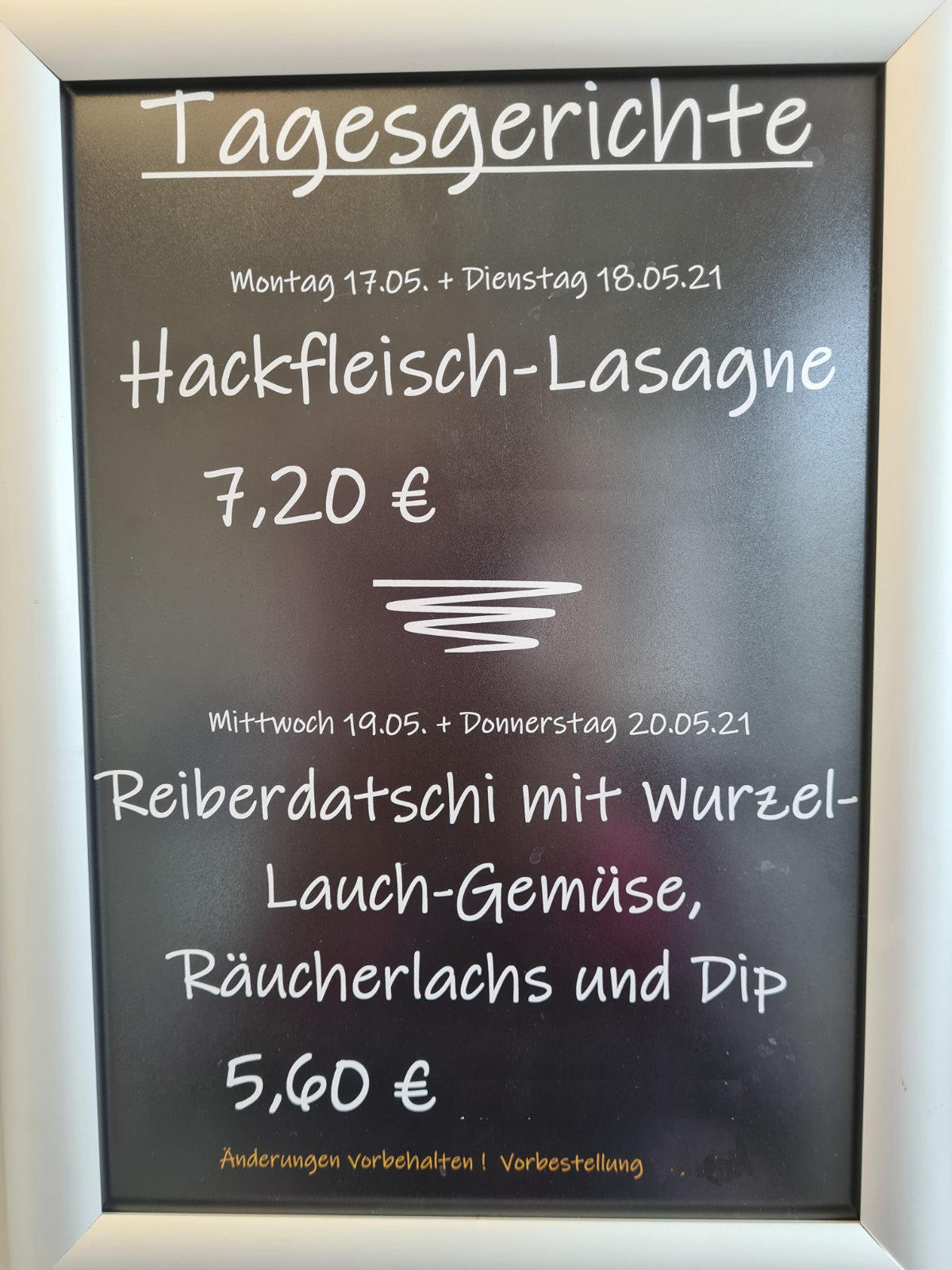 Schwarze Tafel mit silbernem Rahmen und wei&szlig;er Kreideschrift: &Uuml;berschrift 'Tagesgerichte'. Eintr&auml;ge: 'Montag 17.05. + Dienstag 18.05.21 Hackfleisch-Lasagne 7,20 &euro;', Trennstrich, 'Mittwoch 19.05. + Donnerstag 20.05.21 Reiberdatschi mit Wurzel-Lauch-Ge