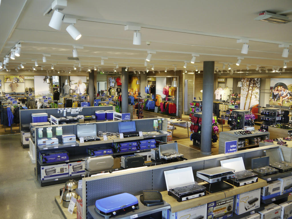 Innenraum eines Gesch&auml;fts mit Auslagetischen, Koffern, Elektronikger&auml;ten, Kleidung an St&auml;ndern und Deckenspots