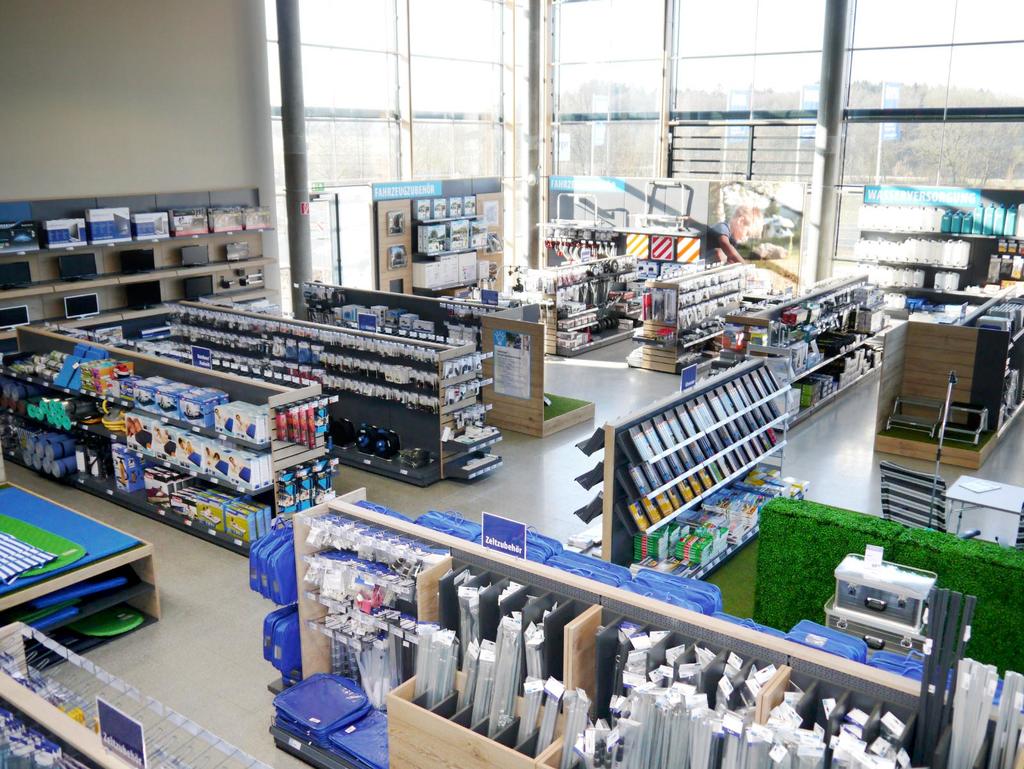 Innenaufnahme eines gro&szlig;en Ladenraums mit langen Regalen, gef&uuml;llten G&auml;ngen und gro&szlig;en Glasfenstern