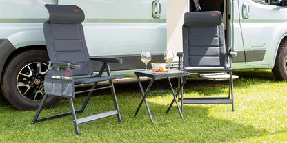 Wei&szlig;es Fahrzeug auf Gras, davor zwei graue Klappst&uuml;hle und ein Klapptisch mit zwei Tassen und weiteren Gegenst&auml;nden