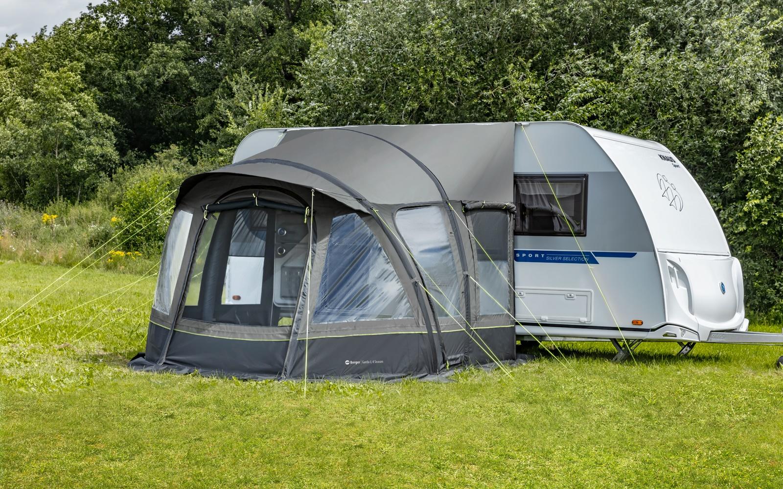 Wei&szlig;er Wohnwagen mit grauem Luftvorzelt auf einer Wiese, B&auml;ume im Hintergrund