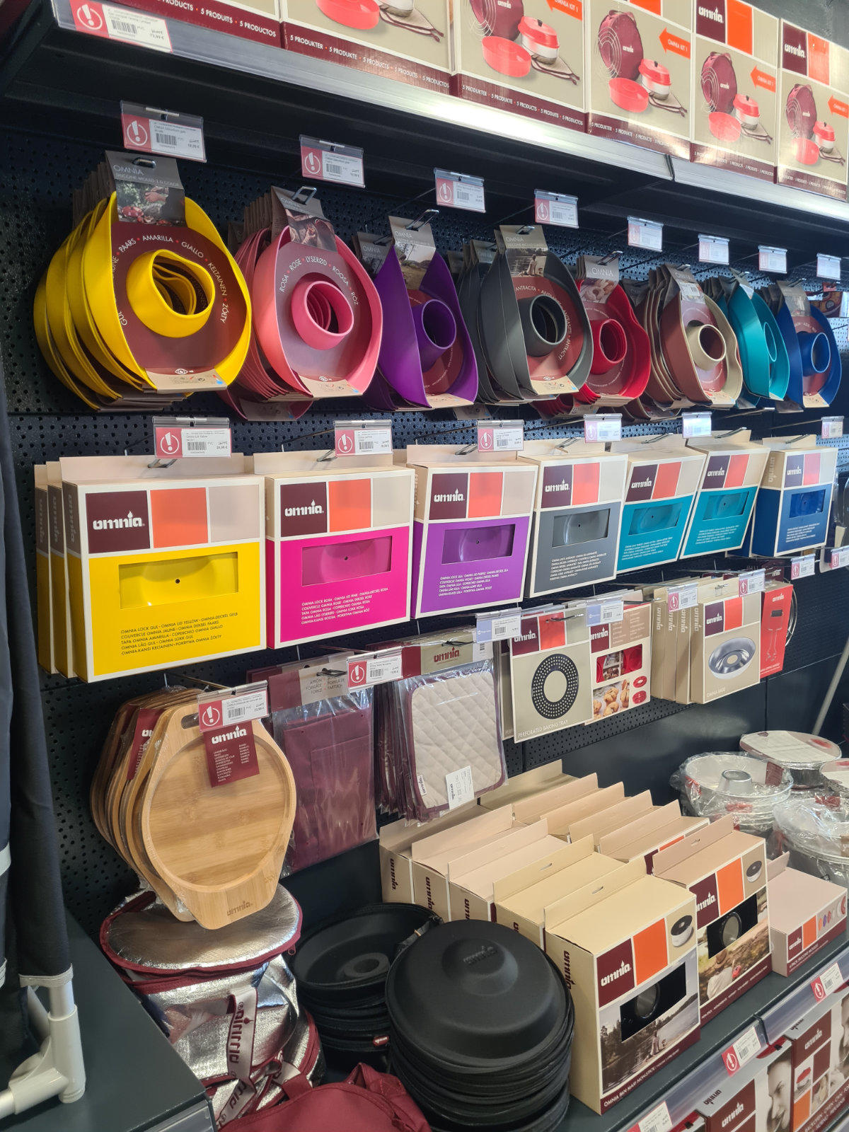 Regal mit aufgeh&auml;ngten bunten runden K&uuml;chenringen, farbigen rechteckigen Verpackungen, runden Holzschneidebrettern und gestapelten schwarzen Pfannen