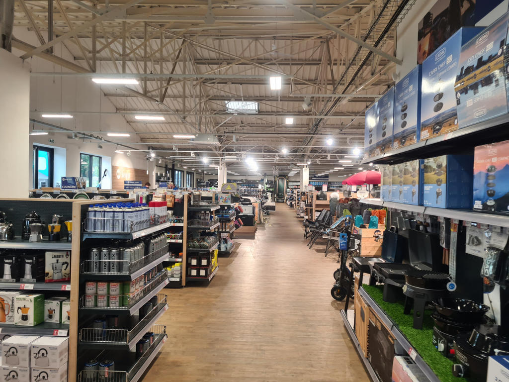 Innenansicht eines gro&szlig;en Ladens mit mittigem Gang, Regalen links und rechts, Deckenbeleuchtung und Holzboden