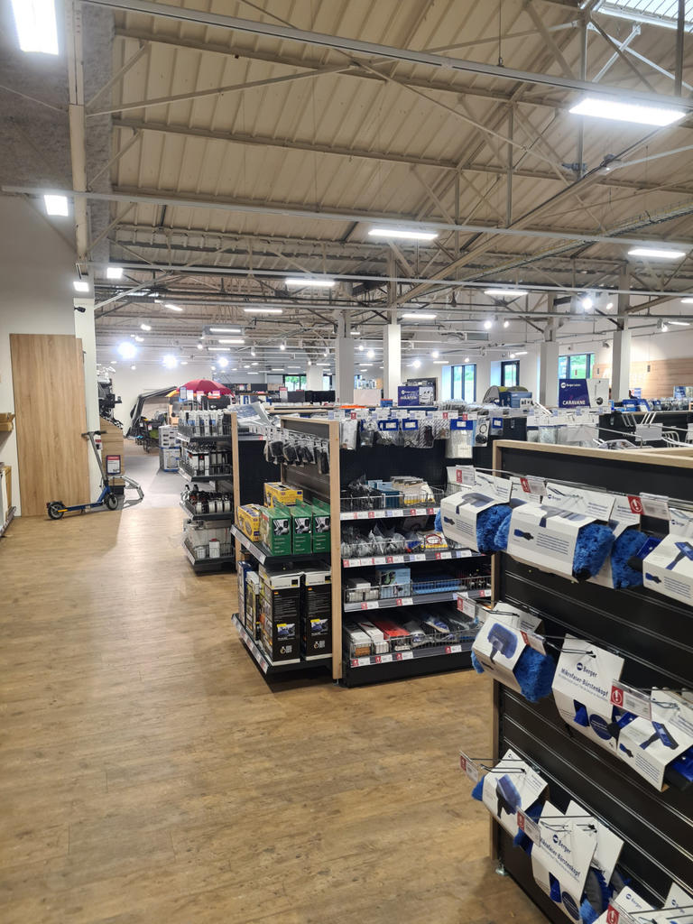 Innenansicht eines gro&szlig;en Gesch&auml;fts mit sichtbaren Metalltr&auml;gern an der Decke, Reihen niedriger Regale mit verpackten Waren, breitem Mittelgang, Holzfu&szlig;boden und Deckenleuchten