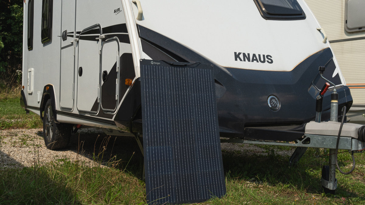 Wei&szlig;er Wohnwagen mit schwarzer Front und KNAUS-Schriftzug auf Gras, ein Solarmodul lehnt gegen die Vorderseite, Anh&auml;ngerkupplung sichtbar