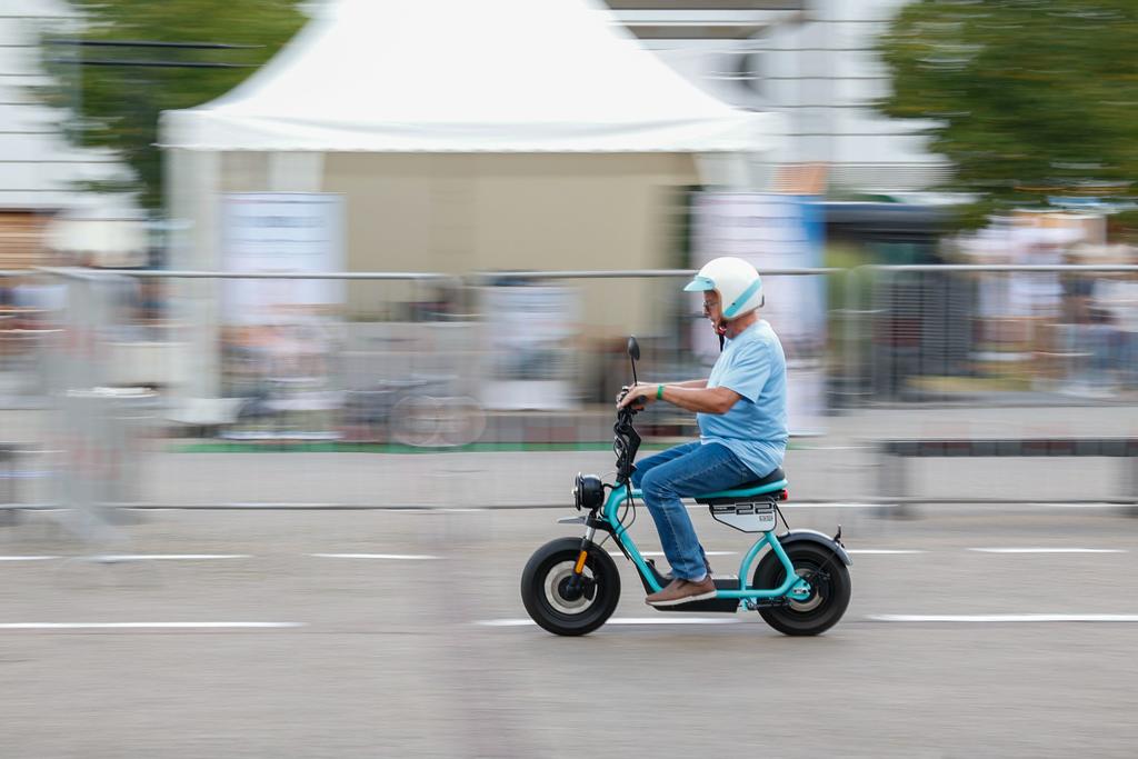 Person mit Helm auf kleinem Elektroroller auf der Straße, unscharfer Hintergrund durch Bewegung