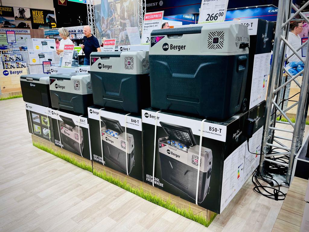 Drei Berger-Kühlboxen auf ihren Kartons nebeneinander, Preisschilder, Kabel, Personen im Hintergrund