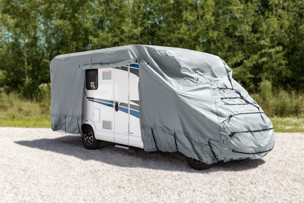 Wei&szlig;es Wohnmobil mit blauen Streifen, mit grauer Plane bedeckt, geparkt auf Kies vor B&auml;umen