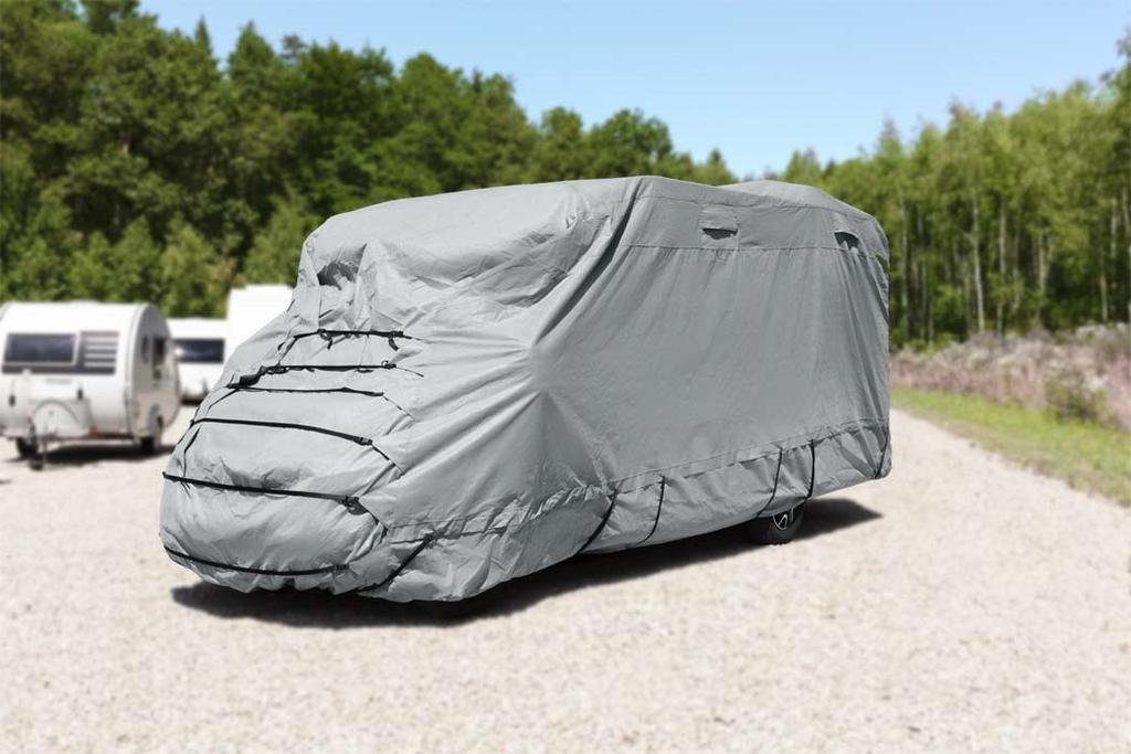 Gro&szlig;es Fahrzeug vollst&auml;ndig mit grauer Abdeckplane bedeckt auf Kiesfl&auml;che, B&auml;ume im Hintergrund und ein links teilweise sichtbarer wei&szlig;er Anh&auml;nger