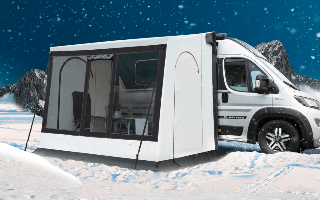 Wei&szlig;er Campingbus mit angebautem wei&szlig;em Vorzelt auf verschneiter Fl&auml;che, im Hintergrund schneebedeckte Berge und ein sternklarer Himmel