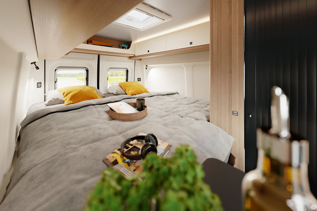 Doppelbett mit grauer Bettdecke und gelben Kissen in einem Wohnmobil, Fenster und Dachluke, Holzschr&auml;nke, Tablett mit Handtuch, Kopfh&ouml;rer und kleine gr&uuml;ne Pflanze im Vordergrund