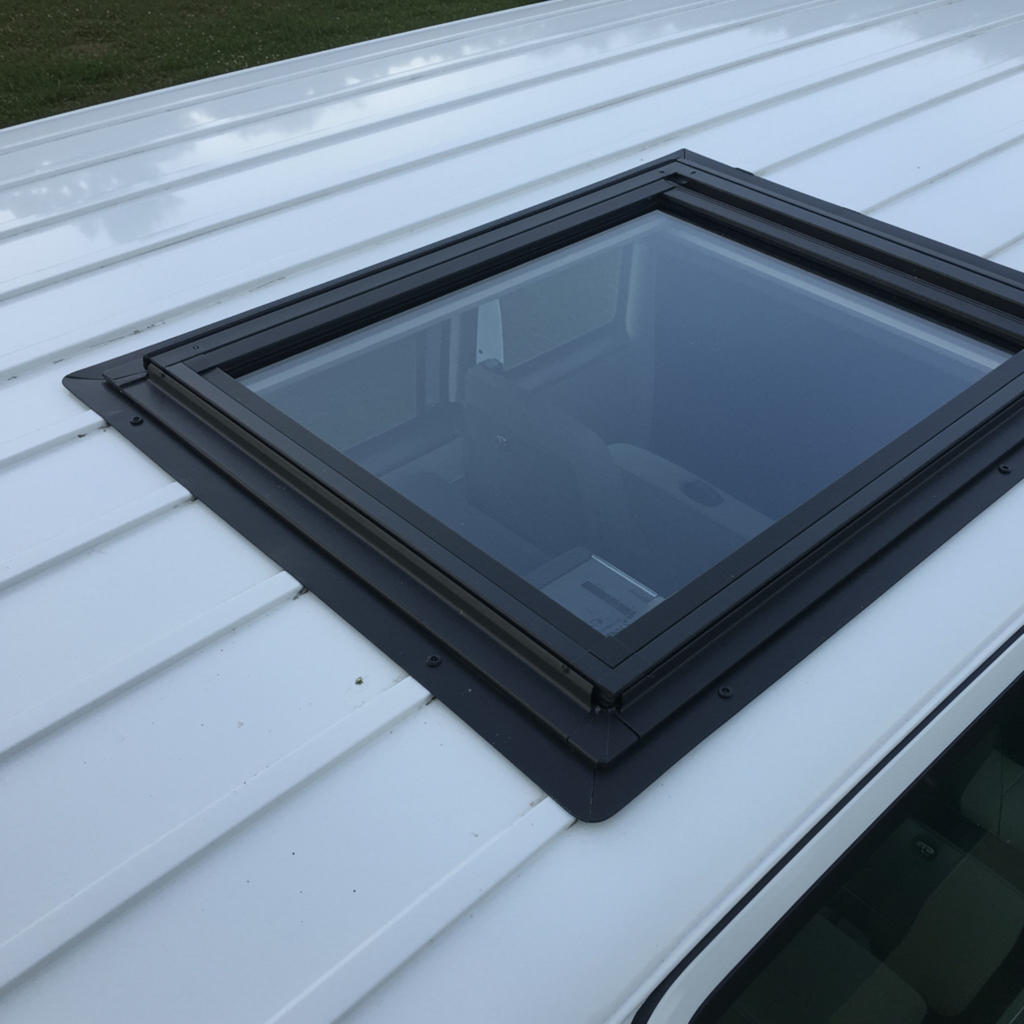 Weißes, profiliertes Dach mit rechteckigem Glasfenster in schwarzem Rahmen; unten Fahrzeugscheibe sichtbar
