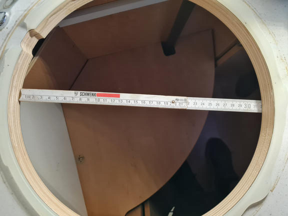 Circular white opening with visible wooden interior; a ruler lies across the opening