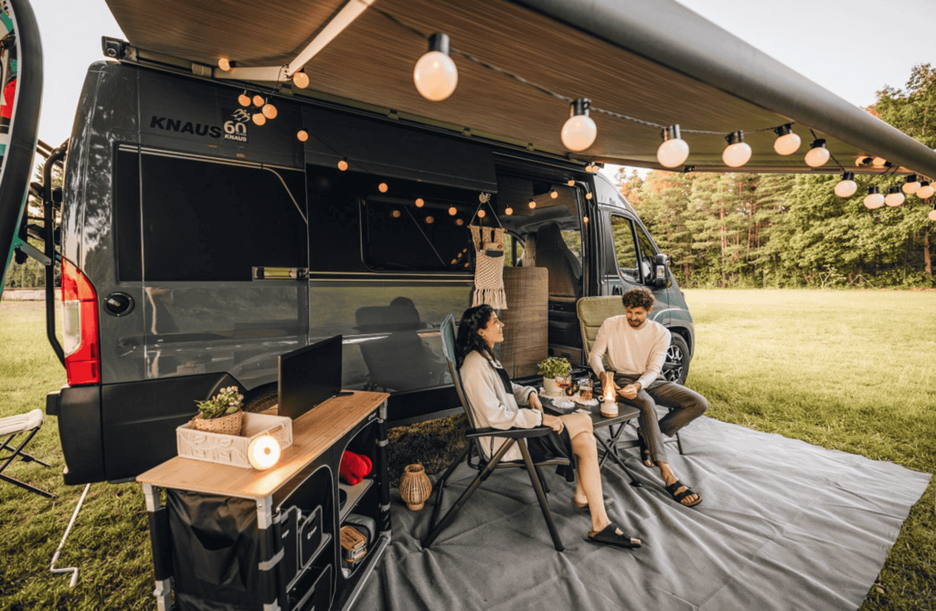 Paar auf Campingstühlen vor Kastenwagen auf Wiese