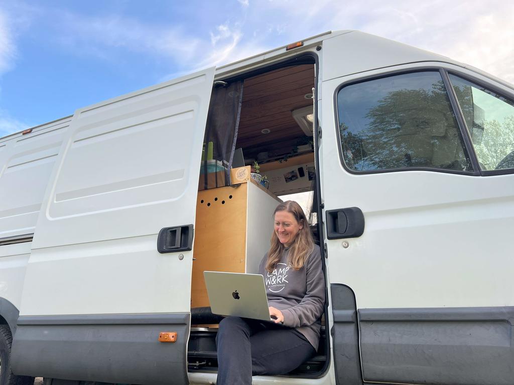 Frau sitzt in ge&ouml;ffneter Schiebet&uuml;r eines wei&szlig;en Vans, mit offenem Laptop auf dem Scho&szlig; und sichtbarer Holzinnenausstattung