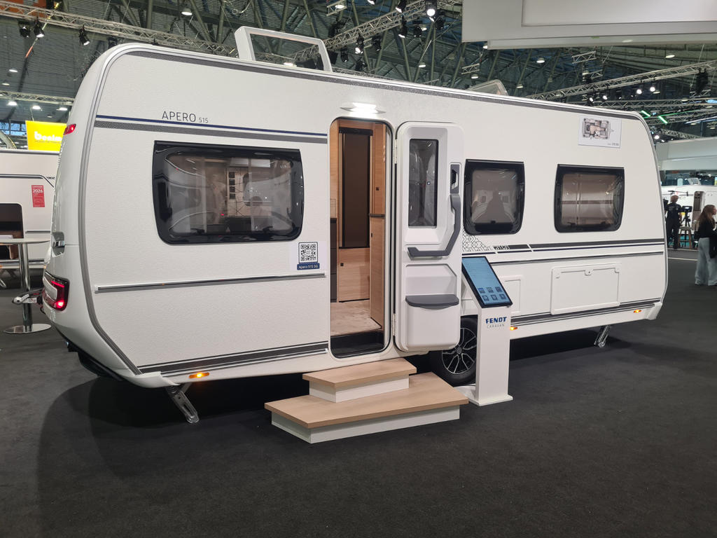 Wei&szlig;er Wohnwagen in gro&szlig;er Halle, ge&ouml;ffnete Eingangst&uuml;r, zwei Auftritts‑Stufen vor der T&uuml;r, Informationsdisplay neben dem Eingang