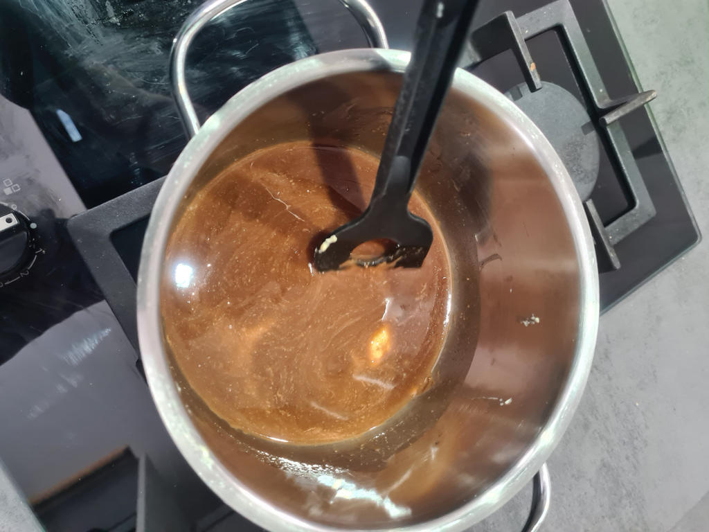 Edelstahltopf auf Herd mit brauner Fl&uuml;ssigkeit und schwarzem Kochl&ouml;ffel