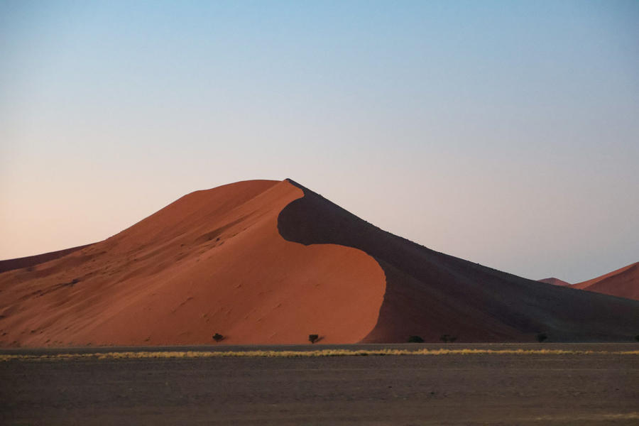 Gro&szlig;e rote Sandd&uuml;ne mit deutlicher Schattenseite, flachem sandigem Vordergrund und klarem blauem Himmel