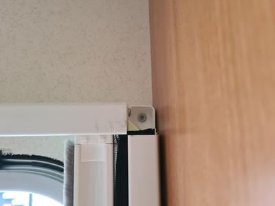 Obere Ecke eines wei&szlig;en Kunststoffrahmens mit Metallwinkel und sichtbarer Schraube, schwarzer Dichtung, helles Deckensegment und Holzverkleidung rechts