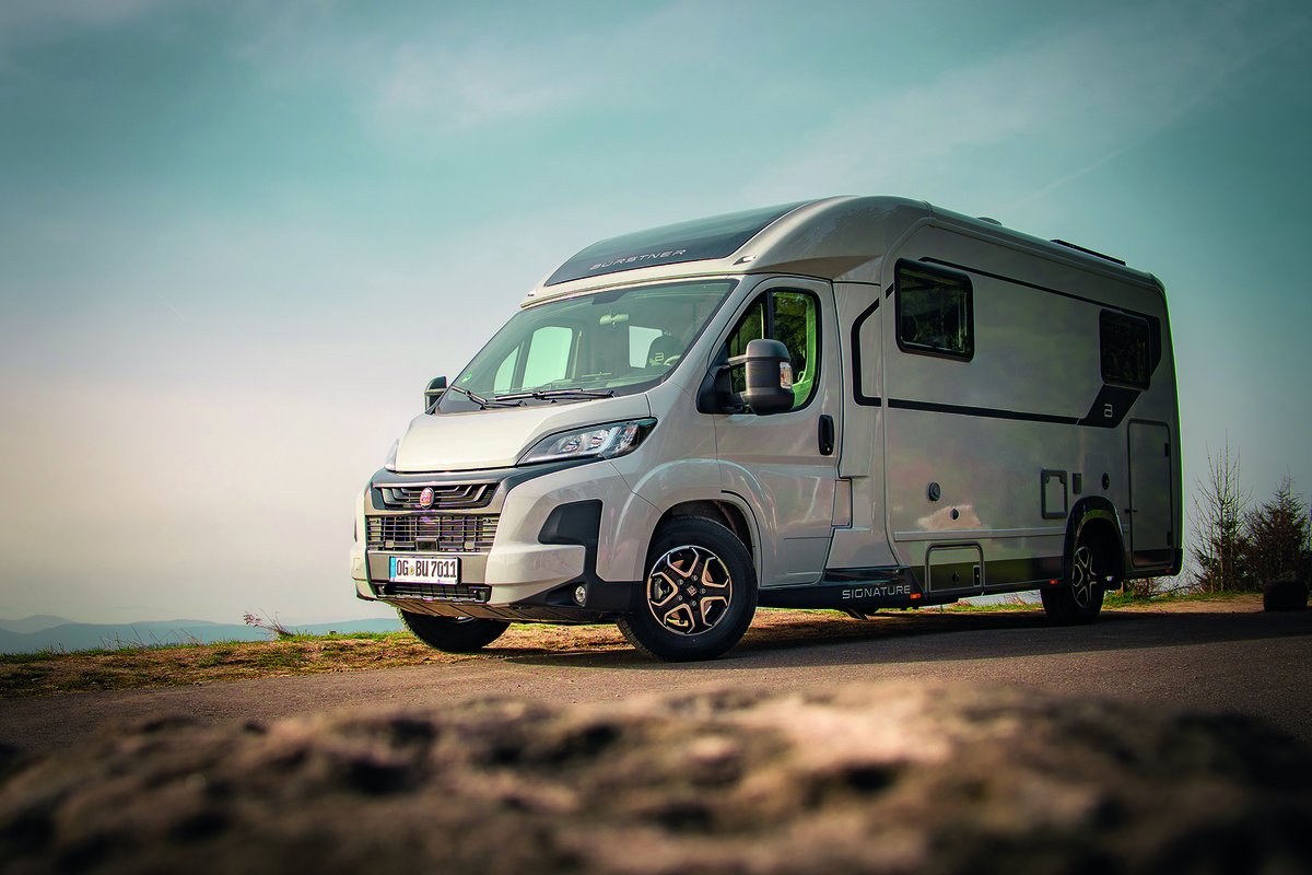 Wei&szlig;es Wohnmobil auf einer Stra&szlig;e, im Vordergrund Felsen, im Hintergrund Himmel und H&uuml;gel