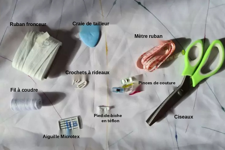 Fournitures de couture sur tissu blanc : bande pour rideaux, craie de tailleur, mètre ruban, ciseaux verts, bobine de fil, crochets de rideau, wonderclips, pied presseur en téflon et aiguille Microtex
