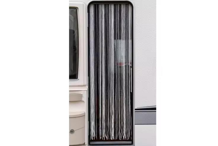 Côté de la porte d'une caravane avec un rideau suspendu à rayures noir et blanc