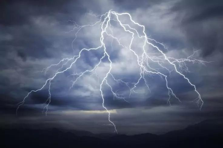 Plusieurs éclairs traversent un ciel sombre et nuageux au-dessus d'une silhouette sombre de montagne