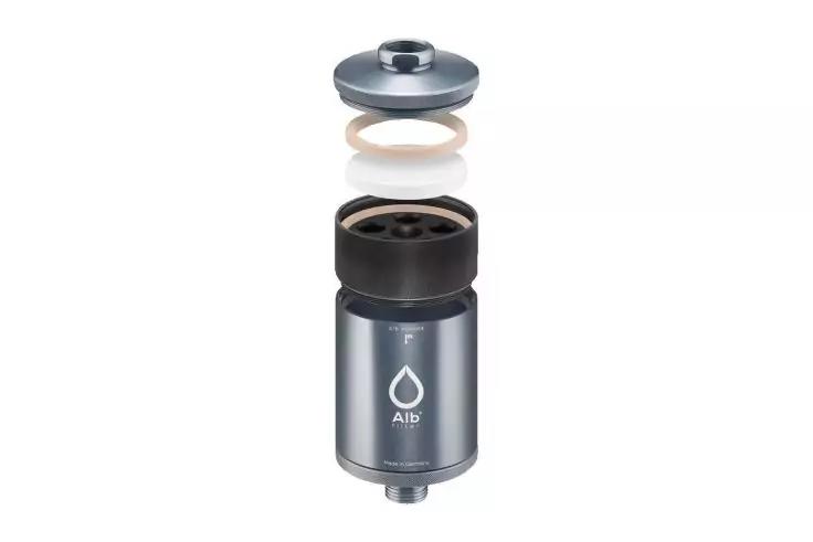 Boîtier métallique cylindrique avec trois pièces flottant au‑dessus : capuchon gris, anneau d'étanchéité blanc, pièce intérieure noire ; symbole de goutte sur le boîtier