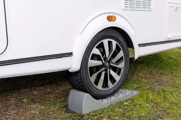 Ruota di una roulotte bianca su un cuneo di livellamento grigio, erba sotto