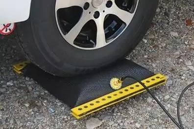 Gomma di automobile su una rampa nera con bordo anteriore giallo, manometro con cavo, superficie ghiaiosa, parte della carrozzeria bianca del veicolo visibile