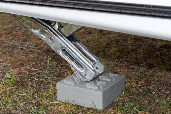 Supporto metallico sotto un veicolo bianco poggia su un blocco in plastica grigio su terreno erboso con rete esagonale