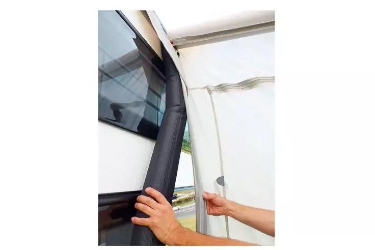 Due mani tengono una guarnizione nera di forma tubolare accanto a un finestrino scuro del veicolo e a una parete di tessuto bianca