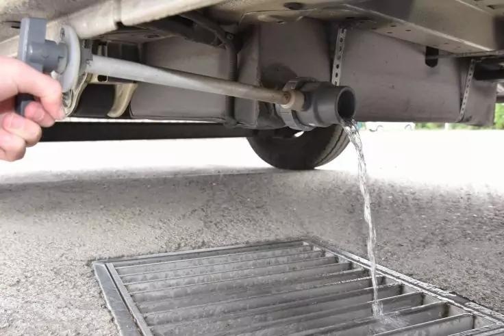 Mano tiene un tubo sotto un veicolo, acqua scorre in una griglia di drenaggio stradale
